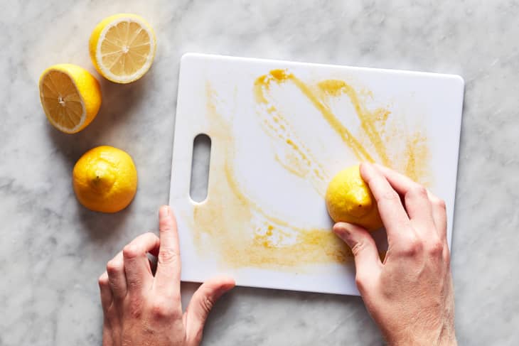 Hand smearing lemon half over dirty plastic cutting board.