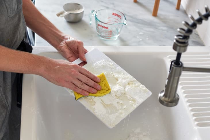 Someone scrubbing plastic cutting board over sink with abrasive sponge.