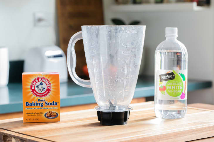 Blender with a cloudy plastic container, with a box of baking soda and bottle of white vinegar, on the kitchen counter