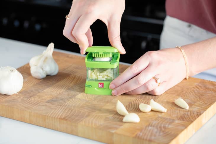 Using garlic press tool to press some garlic on a cutting board