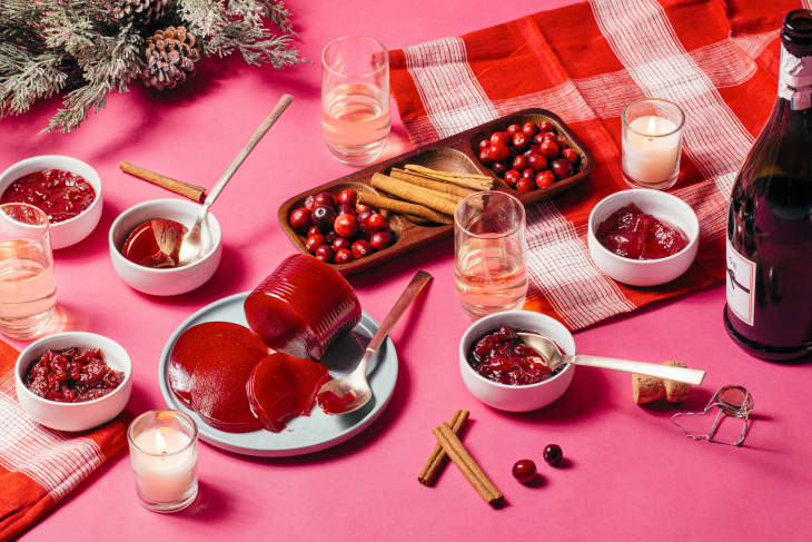 Various cranberry sauces and whole cranberries laid on festive pink table setting.