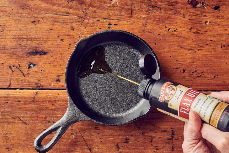 Someone pouring a small amount of flaxseed oil on a dry cast iron skillet.