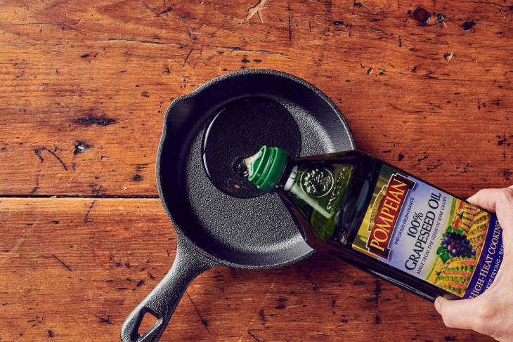 Someone pouring a small amount of grapeseed oil on a dry cast iron skillet.