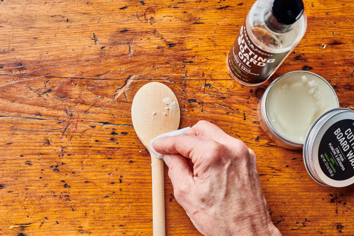 someone applies via paper towel wax to wooden spoon with wax can open near it