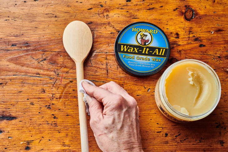 someone applies via paper towel wax to wooden spoon with wax can open near it