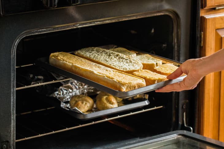 Someone placing garlic bread into the oven.