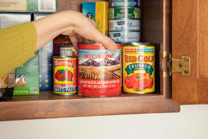 Someone straightening cans in kitchen pantry.