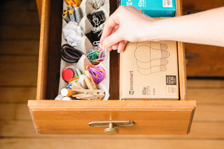 Someone placing paper clips into egg carton to organize junk drawer.