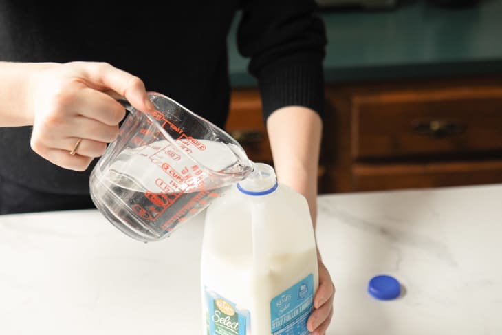 Someone pouring water into jug of expired milk.