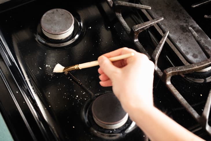 Someone brushing crumbs on stove with paint brush.