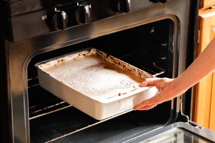 Someone placing casserole dish in oven filled with soapy water.