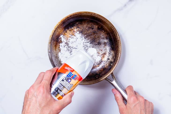 Someone pouring Brillo Cameo powder into stainless steel skillet.