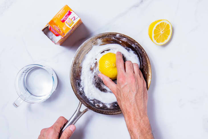 Someone using lemon and baking soda to clean stainless steel skillet.
