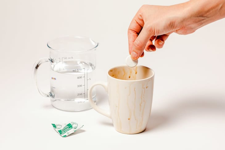 Someone cleaning coffee mug with denture tablet.