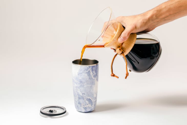 Woman is pouring hot drink from thermos into travel mug