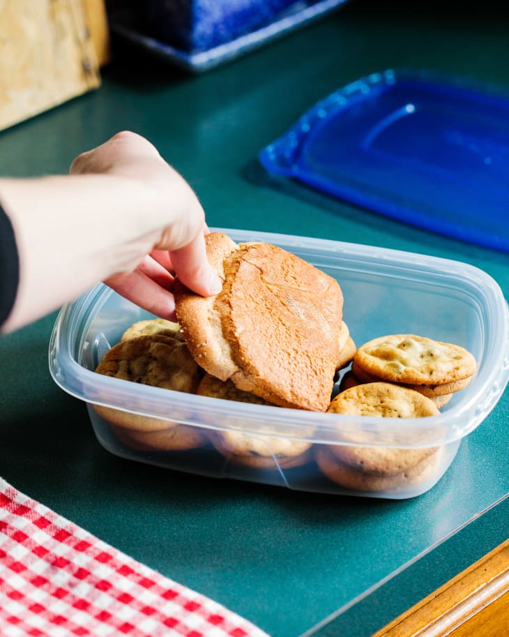 Final piece of bread being placed in tupperware with cookies.