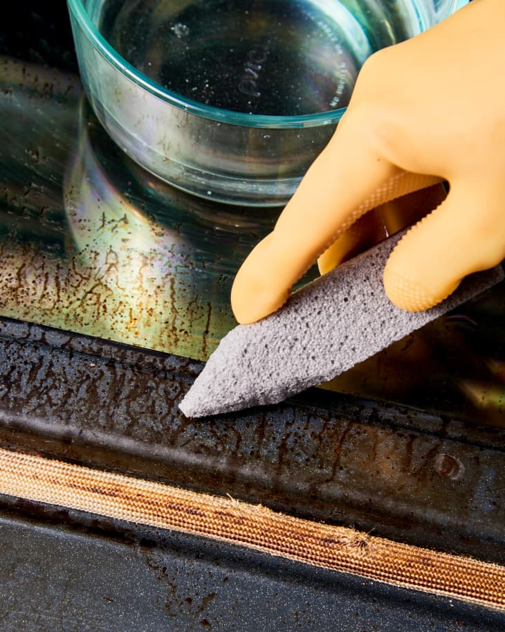 picture of a hand using pumice stone to clean inside of oven