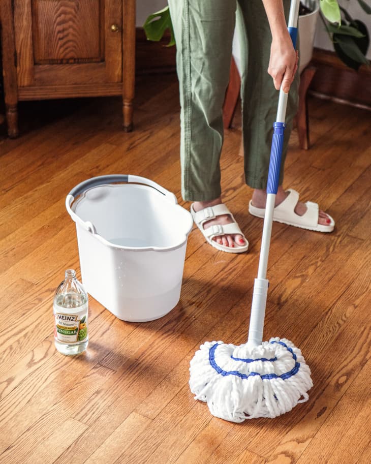 Someone using white vinegar to clean hardwood floor.