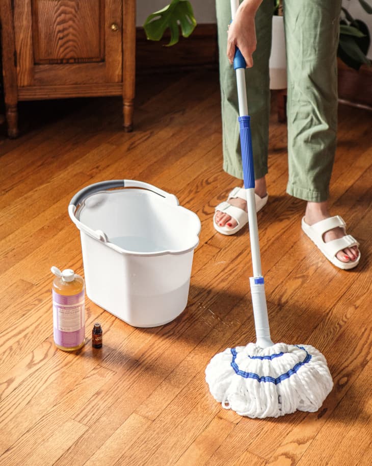 Someone using essential oil and Dr. Bronner's castile soap to clean hardwood floors.