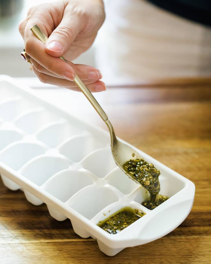 Someone ladling pesto into ice tray to place in freezer.