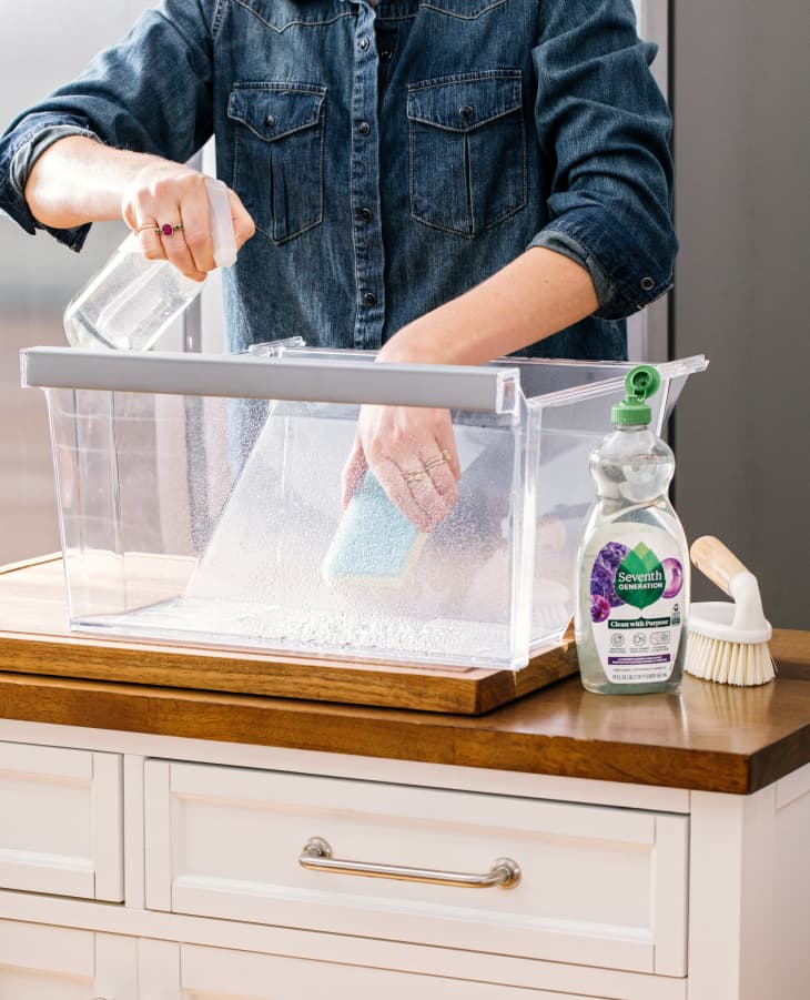Someone using dish soap to clean inside of crisper drawer