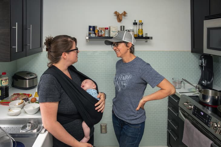 Jodi talks to Robin in their kitchen while Robin holds Eliot in  a baby sling.