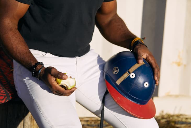 Dale Johnson rests his polo helmet on one knee and holds a half eaten green apple in the other hand.