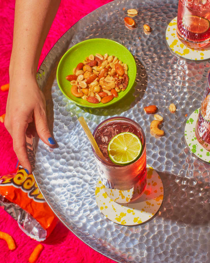 someone holding table with cocktail and green bowl with snacks on it