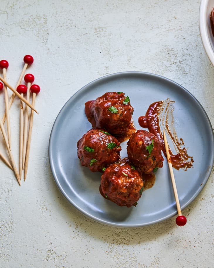 Four BBQ meatballs on a blue-gray plate, with toothpicks next to the plate.