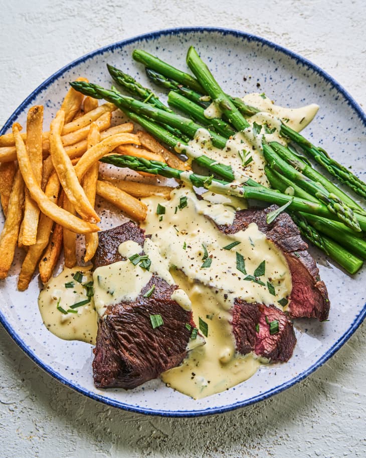 Sliced steak and asparagus with bearnaise sauce poured over the stop, with french fries