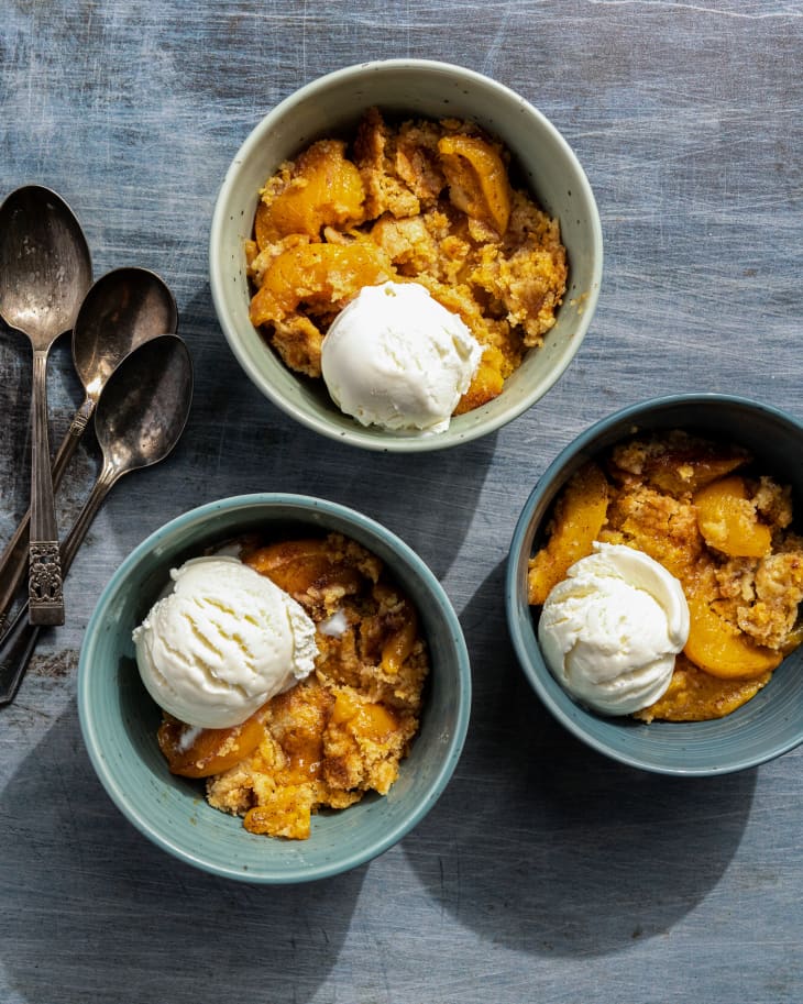 Three portions of Peach Dump Cake scooped out into three bowls, with a scoop of vanilla ice cream on top of each one