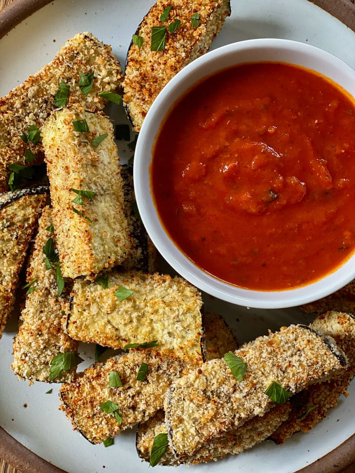 Air Fryer Eggplant on a plate with a small bowl of marinara sauce on the side and a green garnish sprinkled on top.