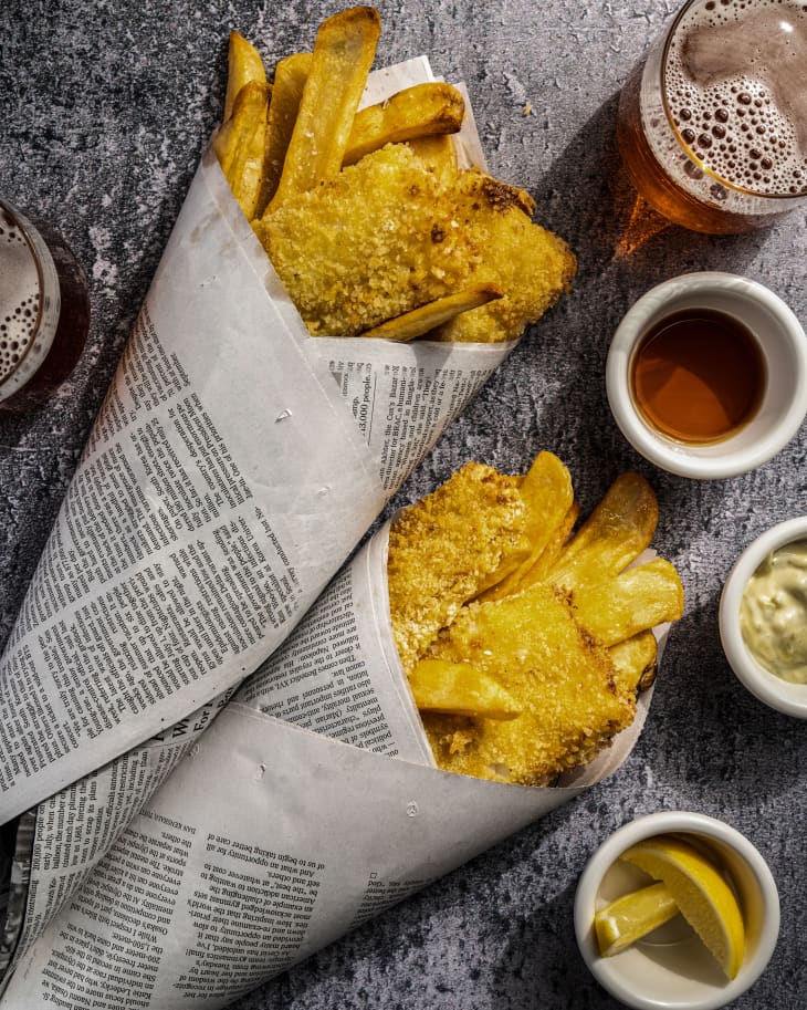 air fryer fish and chips wrapped in newsprint, with sauces and a drink next to them