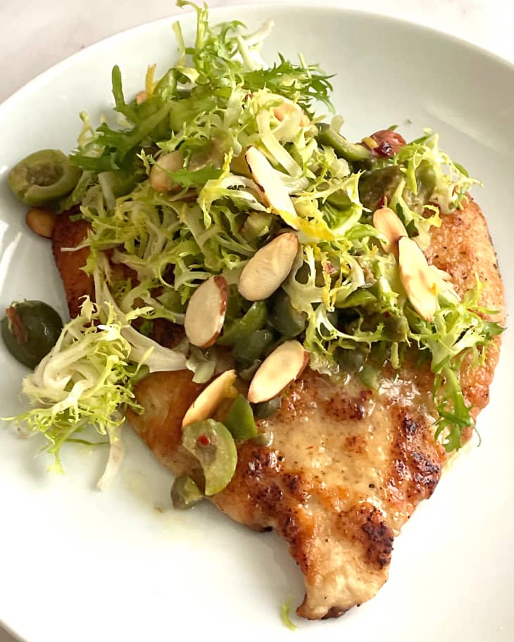 Chicken Paillard on a plate with shredded greens, olives and sliced almonds.