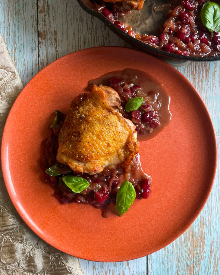 a piece of cranberry chicken on a red plate, on top of a wooden tabletop with a burlap napkin next to it.