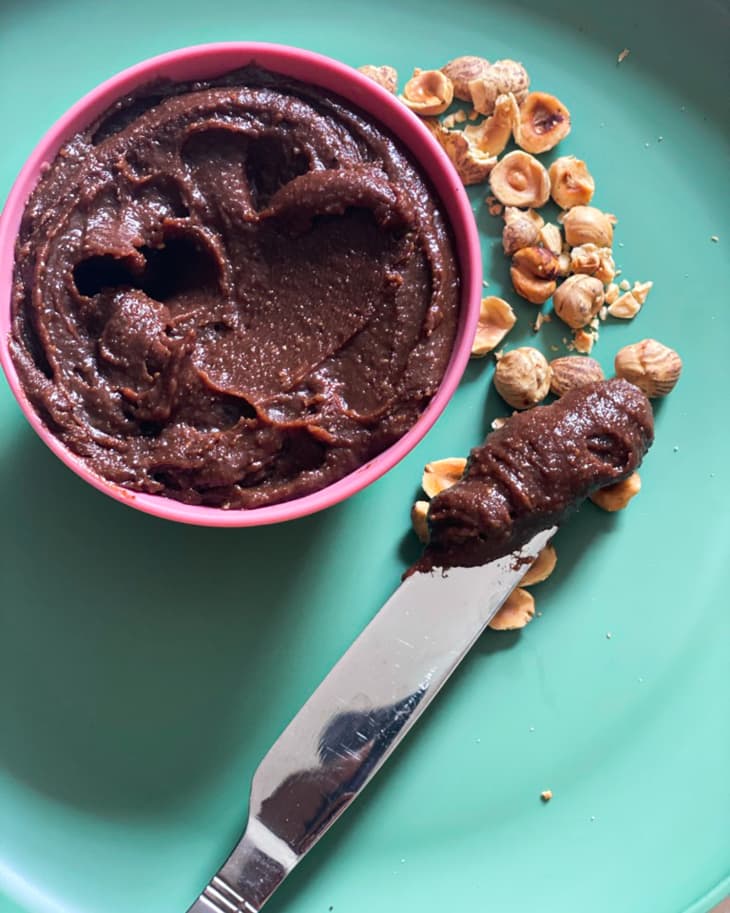 Homemade nutella in a pink bowl with hazelnuts in the background