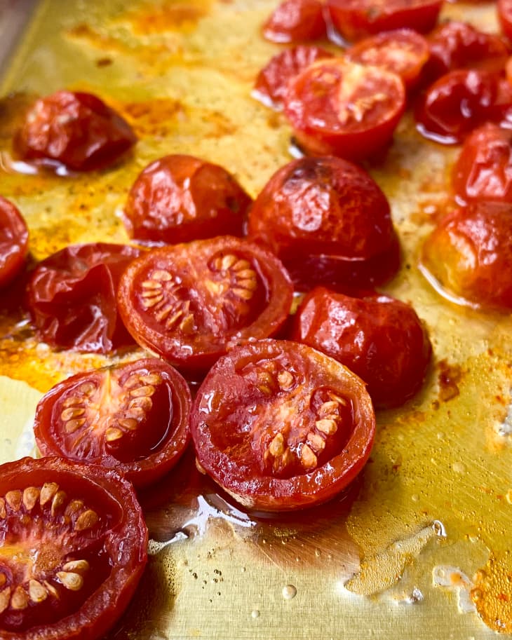 A closeup of roasted cherry tomatoes on a silver baking sheet.