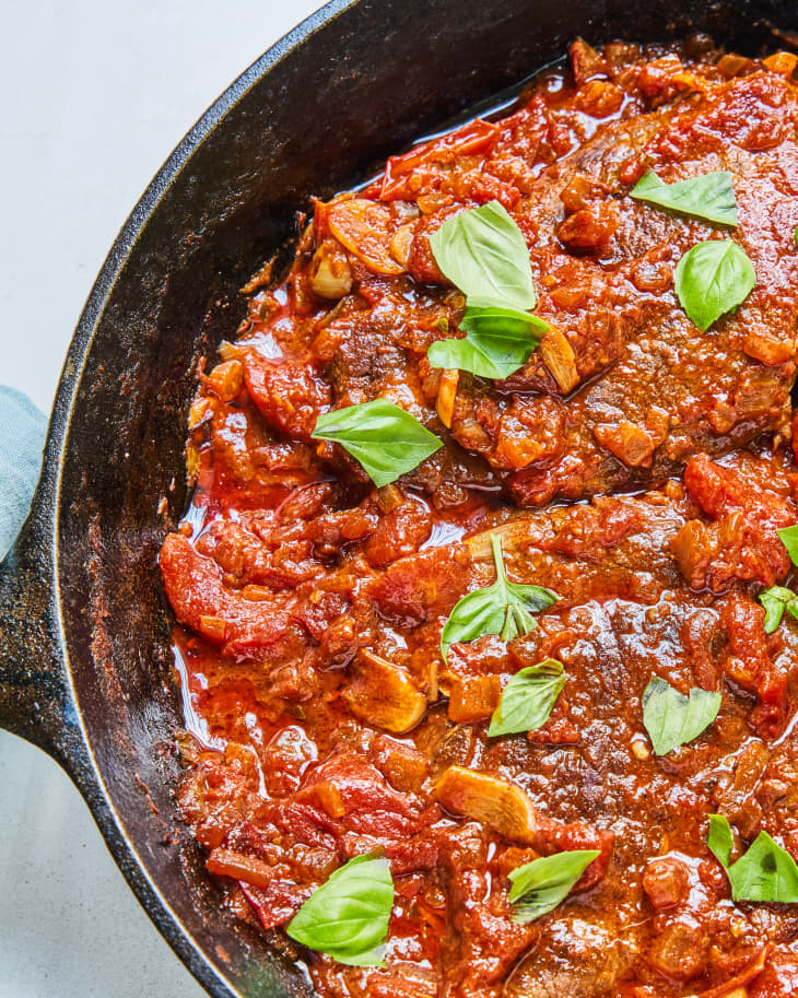 Steak Pizzaiola in a pan with red sauce and basil leaf garnish