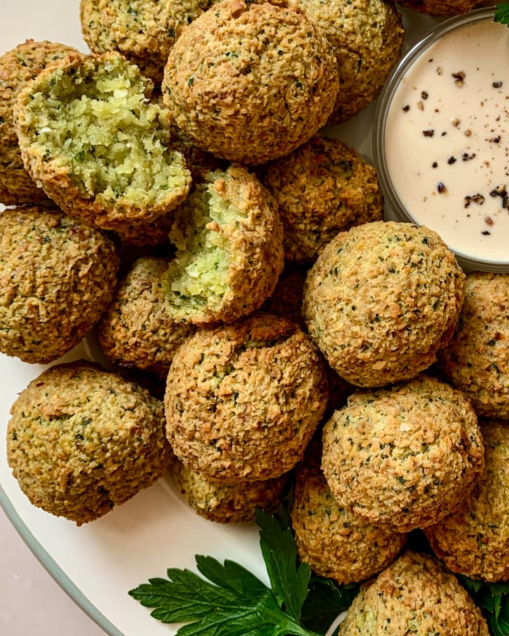 a plate full of air fryer falafel with dipping sauce, with one piece of falafel broken into two pieces.