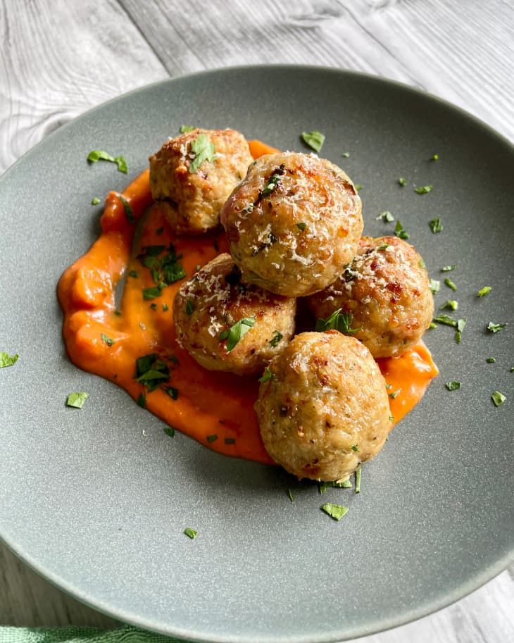 Five baked turkey meatballs on a gray plate, on a bed of red sauce with a green garnish