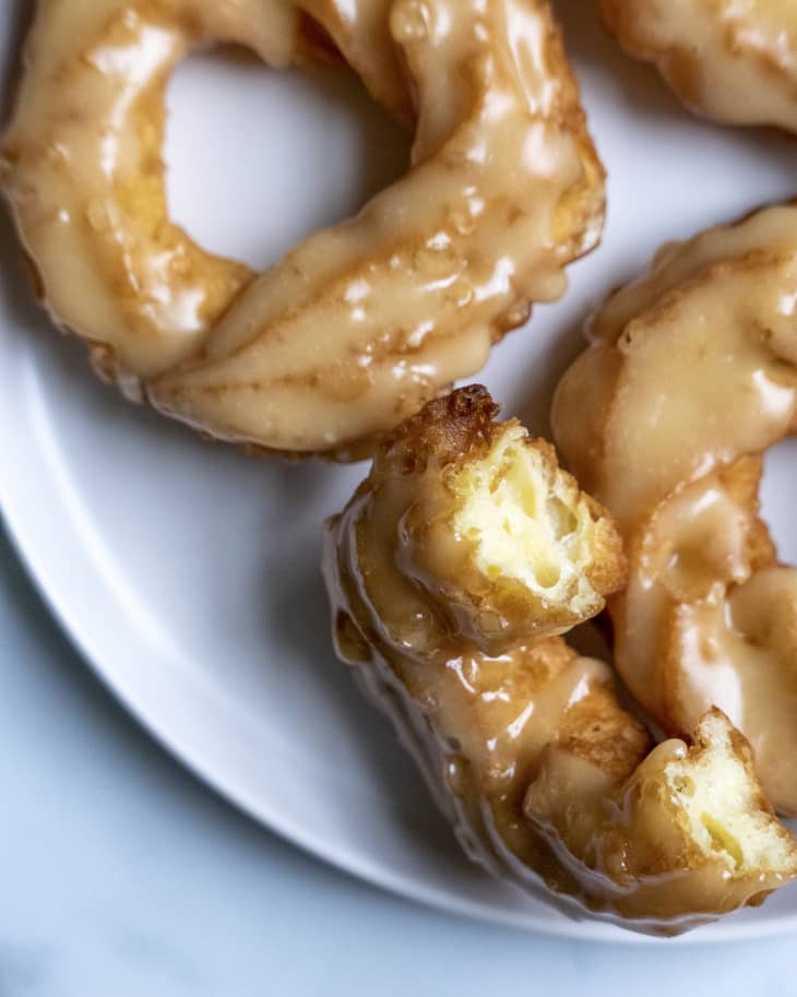 three glazed crullers on a plate, , with one broken in half so that you can see the inside