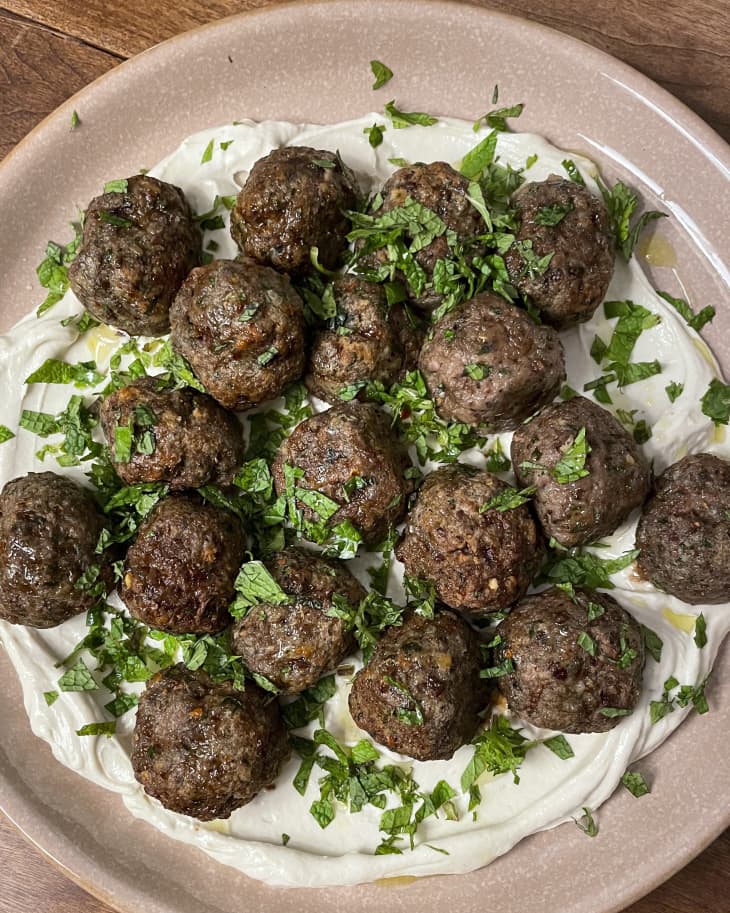 Lamb meatballs on a pale pink plate with white sauce and a green garnish
