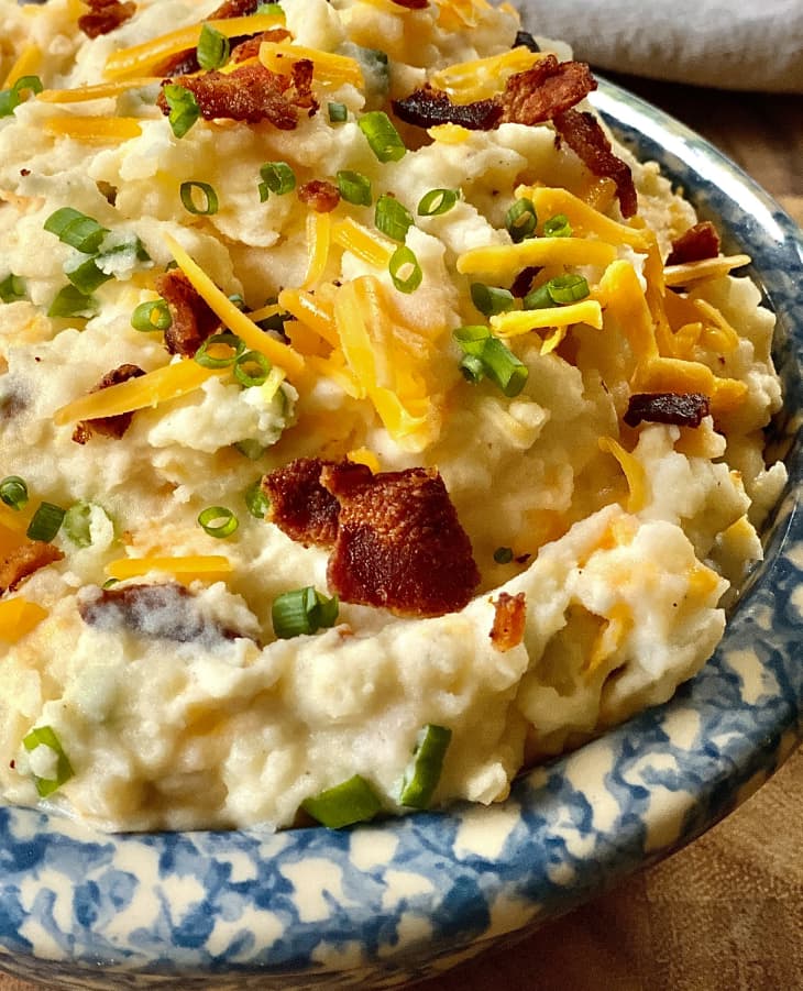 Loaded Mashed Potatoes (mashed potatoes topped with grated cheddar cheese, bacon, green onion) in a blue and white bowl.