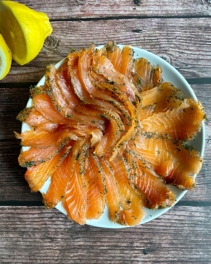 36 Hour cured salmon (lox), sliced on a round plate, with a lemon cut in half on the side.
