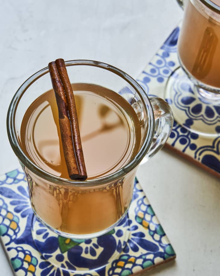 mulled wine with a cinnamon stick on top, in a clear mug, on tile coaster