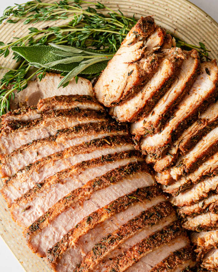 Turkey Tenderloin, roasted and sliced in two rows, on a rounded wooden platter with a rosemary and sage garnish
