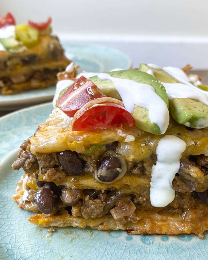 a  square slice of burrito casserole with tomatoes, sliced avocado, jalepeno and sour cream on top.