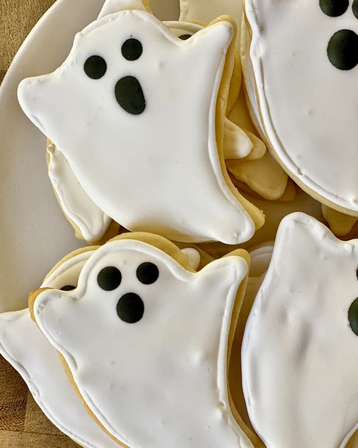 a plate full of ghost-shaped sugar cookies with white icing for the body and black icing for the face