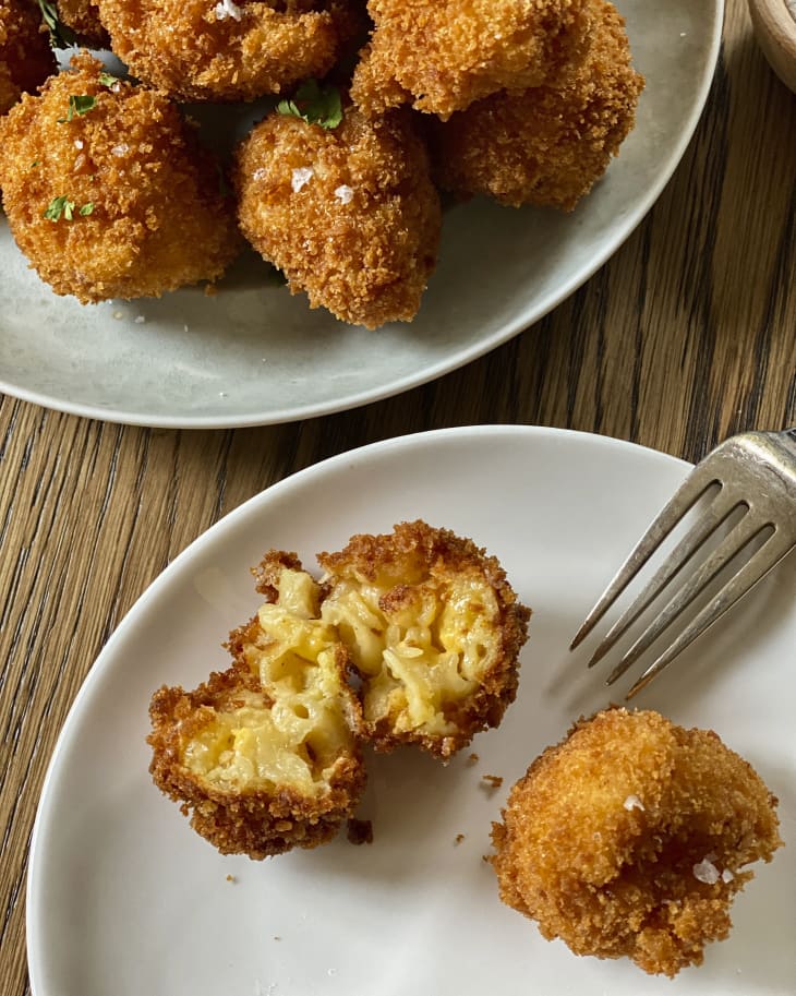 fried mac and cheese balls stacked on a plate with a fork on the side and another plate with two pieces of mac and cheese bites with one split open in half.