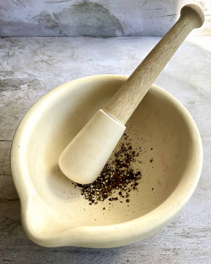 A white ceramic mortar and pestle with ground peppercorns